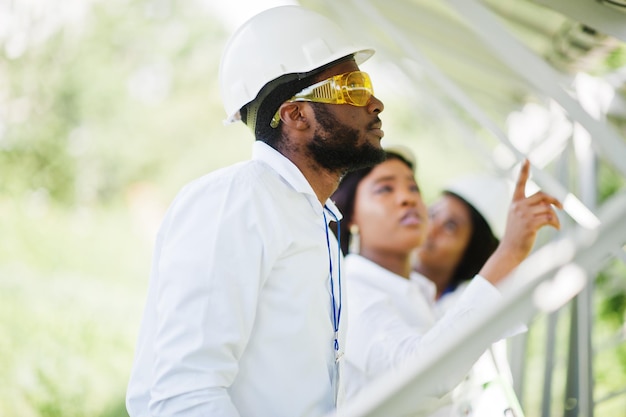 Afroamerikanischer Techniker überprüft die Wartung der Sonnenkollektoren Gruppe von drei schwarzen Ingenieuren, die sich in der Solarstation treffen