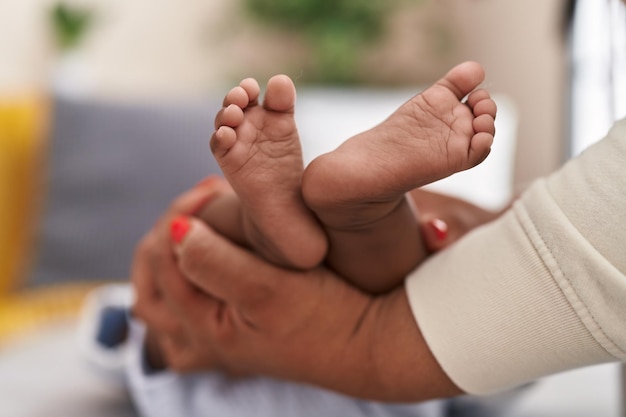 Kostenloses Foto afroamerikanisches baby liegt auf dem bett und lässt sich zu hause die beine massieren