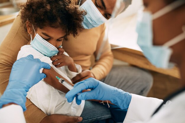 Afroamerikanisches kleines Mädchen, das in einer medizinischen Klinik den COVID19-Impfstoff erhält