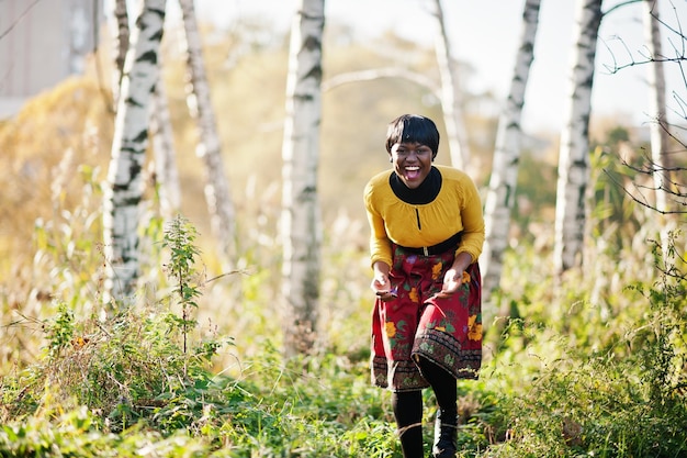 Afroamerikanisches Mädchen im gelben und roten Kleid im goldenen Herbstherbstpark