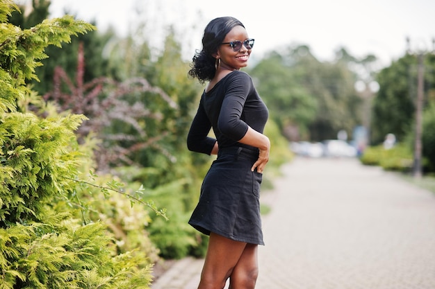 Afroamerikanisches Mädchen mit Sonnenbrille, schwarzer Kleidung und Hemd posierte im Freien Modische schwarze Frau