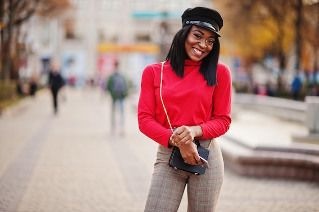 Afroamerikanisches Modemädchen in Zeitungsjungenmütze und Handtasche posierte auf der Straße
