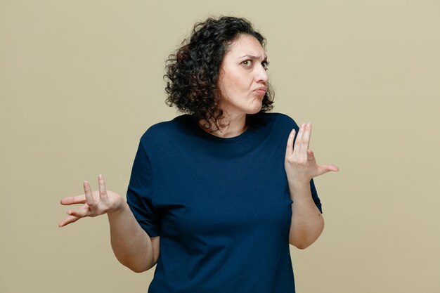 Ahnungslose Frau mittleren Alters, die ein T-Shirt trägt und auf die Seite blickt, die leere Hände isoliert auf olivgrünem Hintergrund zeigt