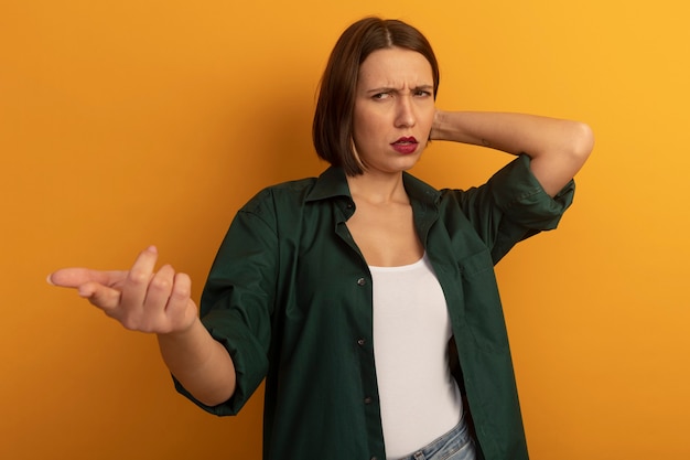 Kostenloses Foto ahnungslose hübsche frau legt hand auf kopf hinter und zeigt zur seite isoliert auf orange wand