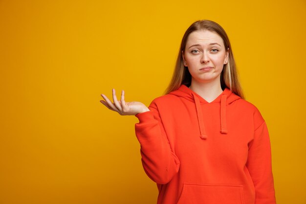 Ahnungslose junge blonde Frau, die leere Hand zeigt