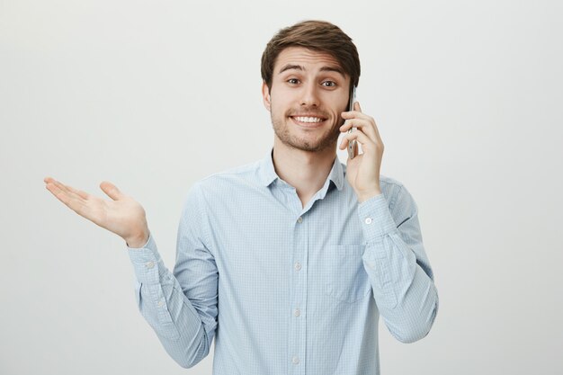 Ahnungsloser süßer Mann mit Borsten, der am Telefon spricht und mit den Schultern zuckt