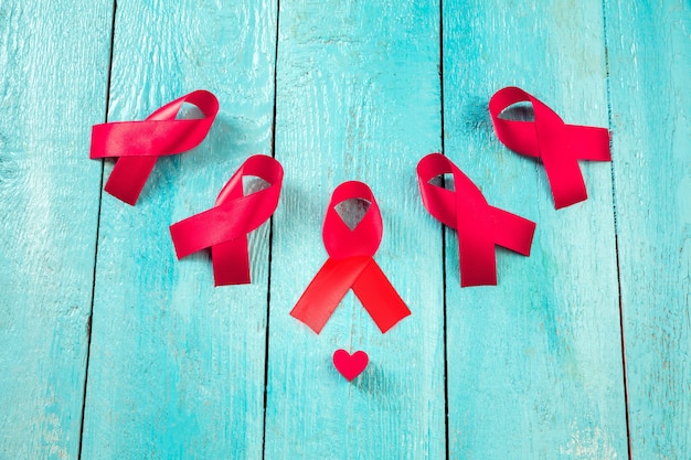Aids Awareness Sign Rote Bänder auf blauem Holzhintergrund. Konzept zum Welt-Aids-Tag. Das Gesundheits-, Hilfe-, Pflege-, Unterstützungs-, Hoffnungs-, Krankheits-, Gesundheitskonzept