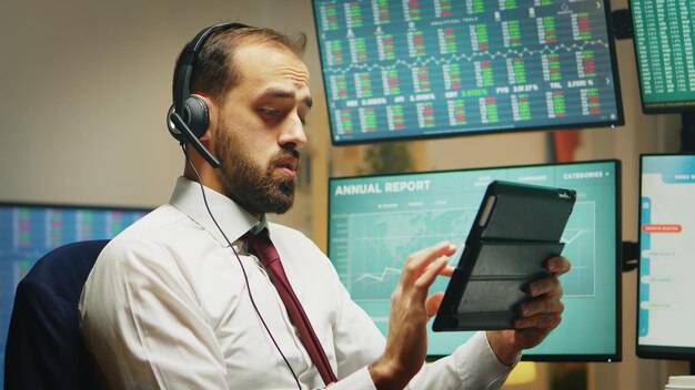 Aktienhändler, die von zu hause aus arbeiten und daten auf einem digitalen tablet überprüfen, während mehrere displays im hintergrund unterschiedliche marktstatistiken anzeigen