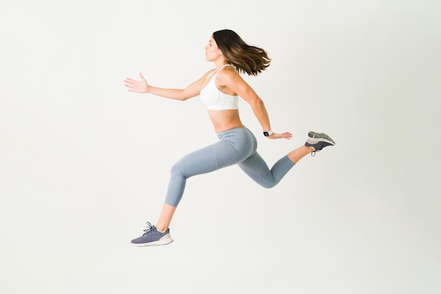 Aktive junge Frau in Sportbekleidung, die in die Luft springt. Sportliche Sportlerin mit starkem Widerstand beim Cardio-Workout und HIIT-Training