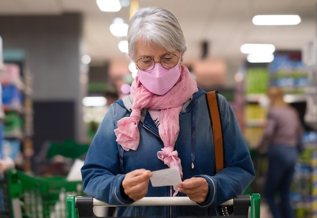 Aktive reife erwachsene seniorin, die im supermarkt einkauft und den einkaufswagen mit ffp2-maske schiebt