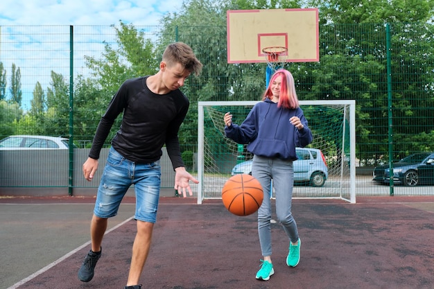 Aktiver gesunder lebensstil der jugend, hobbys und freizeit, teenager kerl und mädchen auf einem basketballplatz im freien, der straßenbasketball spielt