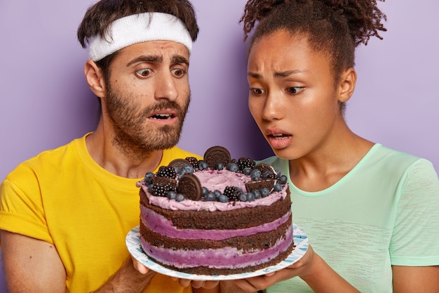 Kostenloses Foto aktives paar posiert mit einem großen kuchen