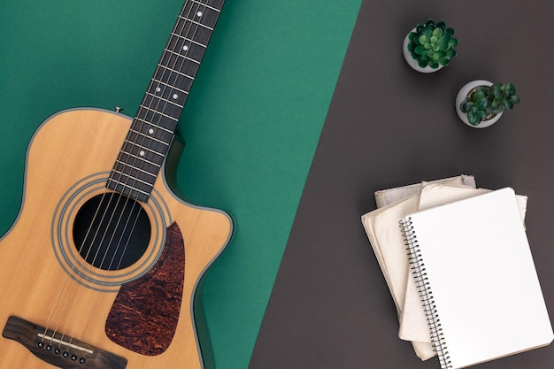 Kostenloses Foto akustikgitarre und leeres notizbuch auf einer draufsicht des farbigen hintergrundes