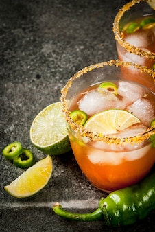 Alkohol. traditionelles mexikanisches südamerikanisches cocktail. würzige michelada mit scharfen jalapenopfeffern und limetten. auf einem dunklen steintisch. copyspace