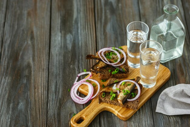 Alkoholisches Getränk mit Fisch und Brot Toast auf Holzwand. Alkohol purer Craft Drink und traditionelle Snacks. Negativer Raum. Feiern und lecker. Draufsicht.