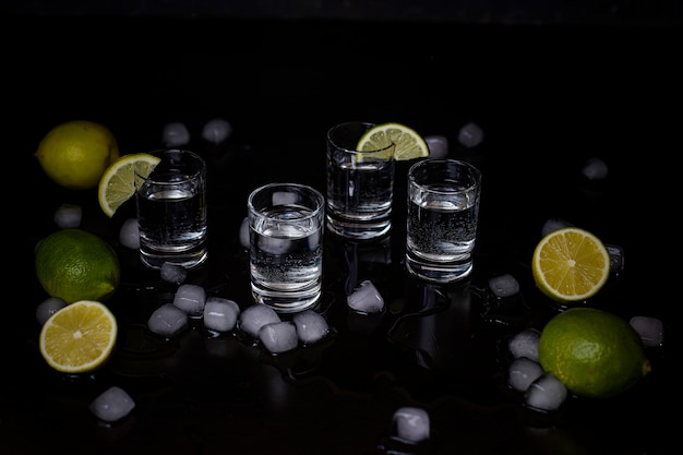 Alkoholschüsse mit Kalk- und Eiswürfeln auf Schwarzem