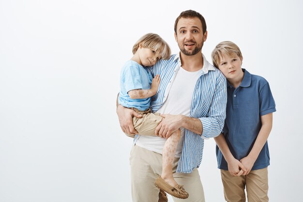 Alleinerziehende, die sich um Söhne kümmern. Vater hält süßes Kind mit Vitiligo, während er nervös starrt, mit zwei Jungen allein gelassen wird, ahnungslos, wie man auf Kinder aufpasst