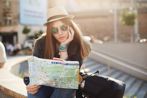 Alleinreisende weibliche Touristen, die eine Karte im Zentrum der europäischen Stadt verwenden. Verlorene Reisen, die verwirrt aussehen und einen Hut tragen
