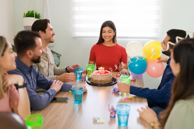 Alles Gute zum Geburtstag! Fröhliche Freunde zu Hause singen und schmeißen eine Geburtstagsfeier mit Kuchen für eine schöne junge Frau