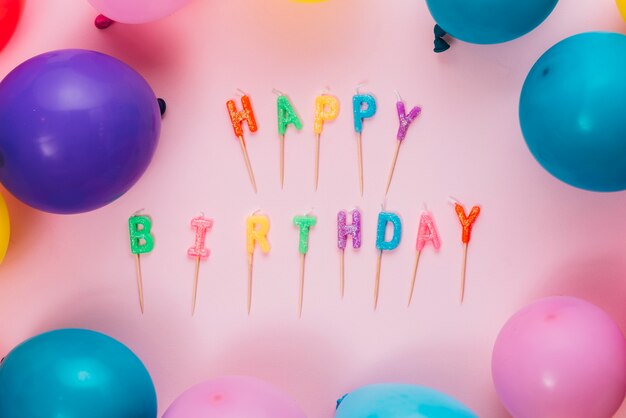 Alles Gute zum Geburtstagkerzen mit bunten Ballonen auf rosa Hintergrund
