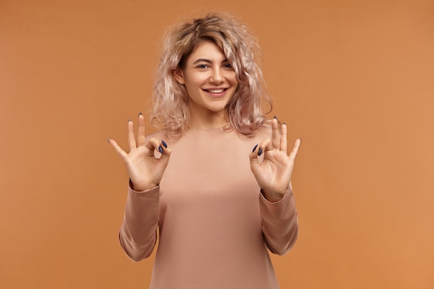 Alles ist perfekt. Horizontal der freundlich aussehenden charmanten jungen Frau mit Piercing im Gesicht und rosa Haaren, die positive Emotionen ausdrücken und breit lächeln