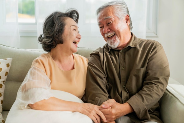Alte ältere asiatische Rentner heiraten Paar Wellness-Lebensstil zusammen zu Hause alte Leute lachen Lächeln zusammen mit Liebe und Verbundenheit auf dem Sofa im Wohnzimmer nach Hause Innenhintergrund