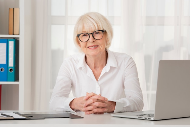 Alte Frau des smiley mit den Brillen, die in ihrem Büro sitzen