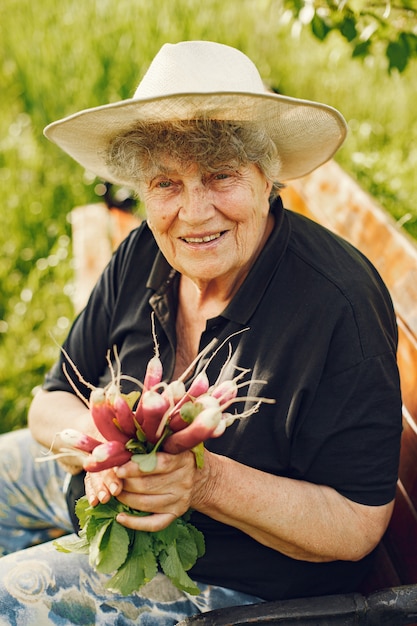 Alte Frau in einem Hut, der frische Radieschen hält