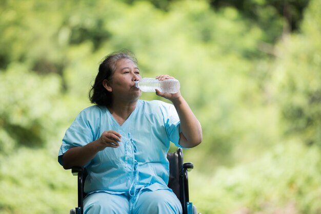 Alte Frau sitzen auf Rollstuhl mit Wasserflasche nach nehmen eine Medizin