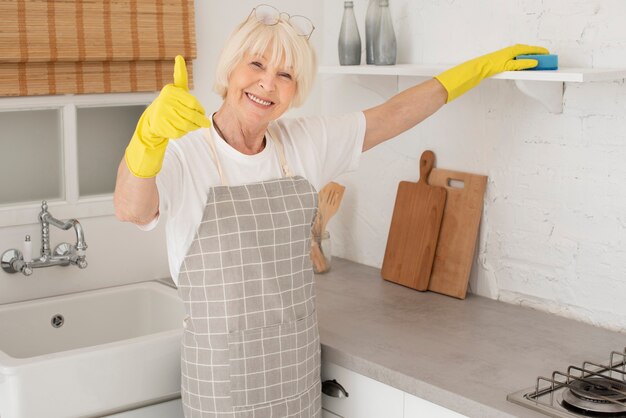 Alte Frau, welche die Küche mit Handschuhen säubert