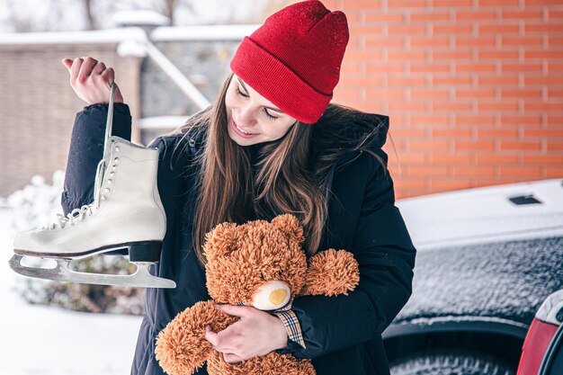 Alte Schlittschuhe und ein Teddybär in den Händen einer jungen Frau im Winter