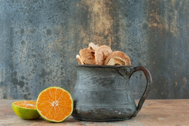 Alte Teekanne voller getrockneter Äpfel mit halb geschnittener Mandarine