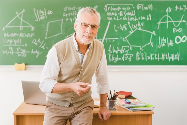 Alter lächelnder Lehrer mit Kreide im Klassenzimmer