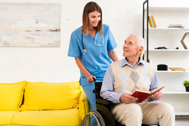 Alter Mann, der auf Rollstuhl bei der Unterhaltung mit Krankenschwester sitzt