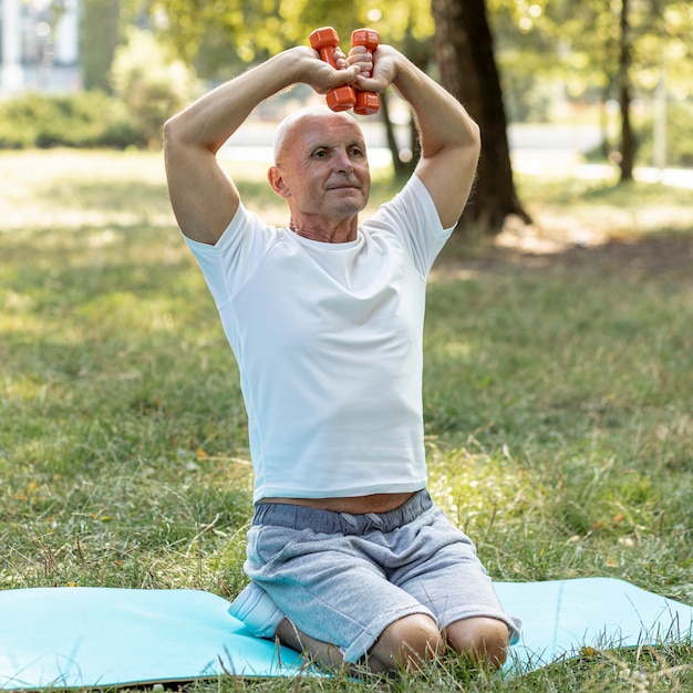 Alter Mann, der auf Yogamatte in der Natur ausarbeitet