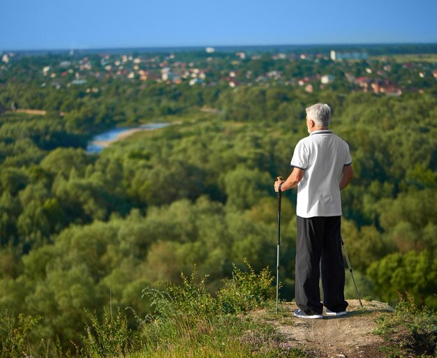 Alter Mann, der das Stadtpanorama beobachtet und Tracking-Sticks hält