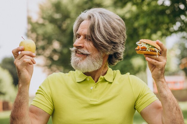 Alter Mann, der zwischen Burger und Apfel wählt