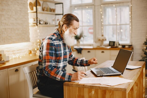 Alter Mann mit Laptop. Großvater sitzt in einer Weihnachtsdekoration. Mann in einem Zellenhemd.