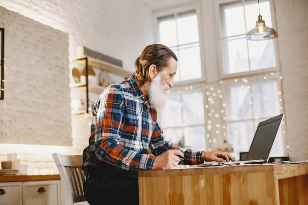 Alter Mann mit Laptop. Großvater sitzt in einer Weihnachtsdekoration. Mann in einem Zellenhemd.