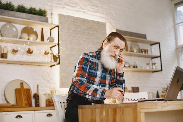 Alter Mann mit Laptop. Großvater sitzt in einer Weihnachtsdekoration. Mann mit Handy.