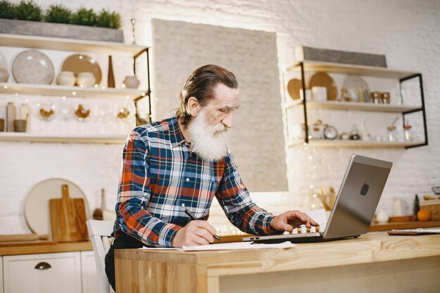 Alter Mann mit Laptop. Großvater sitzt in einer Weihnachtsdekoration.