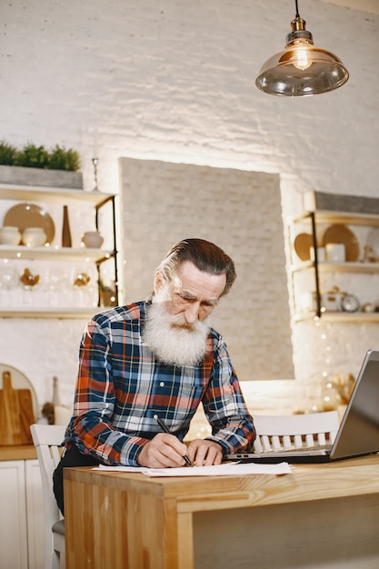 Alter Mann mit Laptop. Großvater sitzt in einer Weihnachtsdekoration.