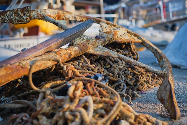 Alter rostiger Anker auf der alten Ankerkette im Jachthafen der Stadt in den Strahlen der aufgehenden Sonne Pier im Yachtclub mit selektivem Fokushintergrund oder Bildschirm über Urlaub und Reisen am Meer