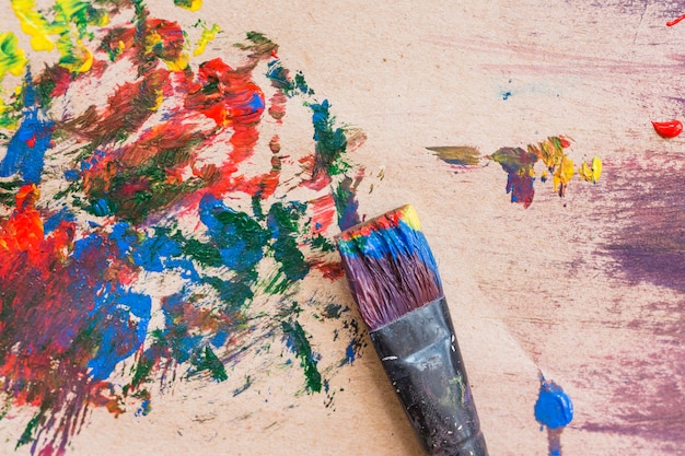 Alter schmutziger Malerpinsel und mehrfarbige unordentliche gemalte Oberfläche