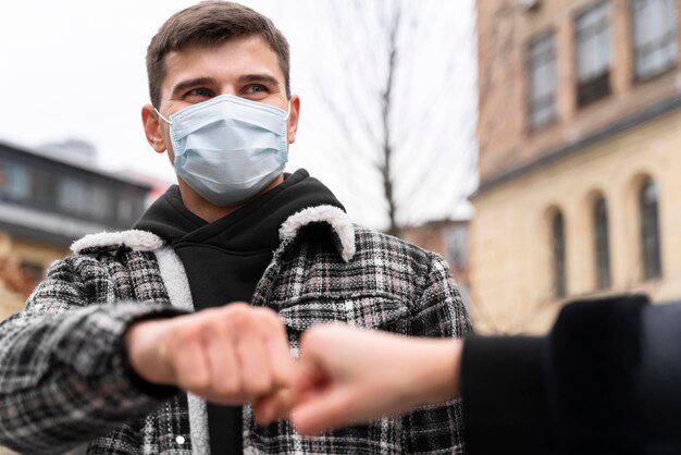 Alternative Grüße, die fast die Faust berühren, stoßen Mann mit Maske an