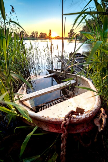 Altes eisernes Ruderboot, das bei Sonnenuntergang teilweise am Ufer eines Teiches versenkt wurde