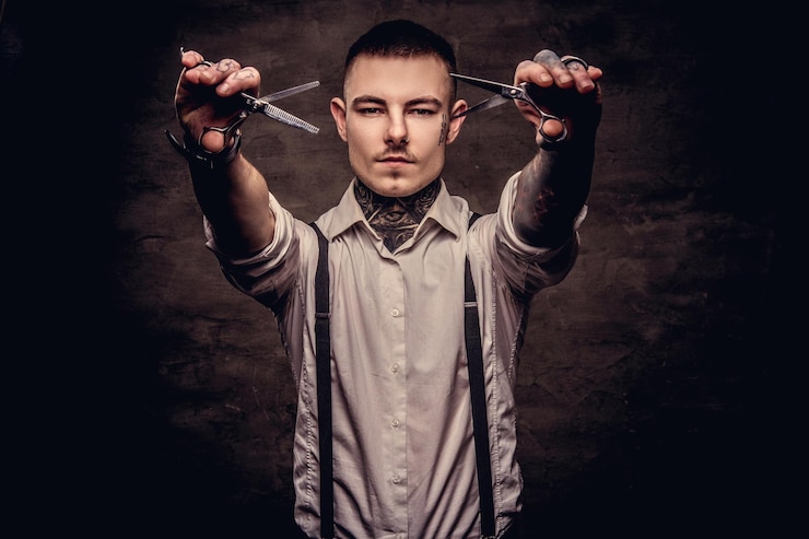 Kostenlose Foto altmodischer tätowierter hipster, der ein weißes hemd mit hosenträgern trägt, hält eine schere. getrennt auf einem dunklen strukturierten hintergrund.