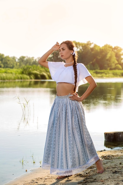 Am Rand des Ufers in der Nähe des Flusses steht ein Mädchen in einem weißen Kleid. Das Konzept der Ruhe im Dorf