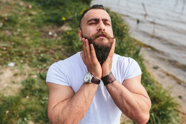 American Bearded Man sieht in einer blauen Jacke am Flussufer aus river