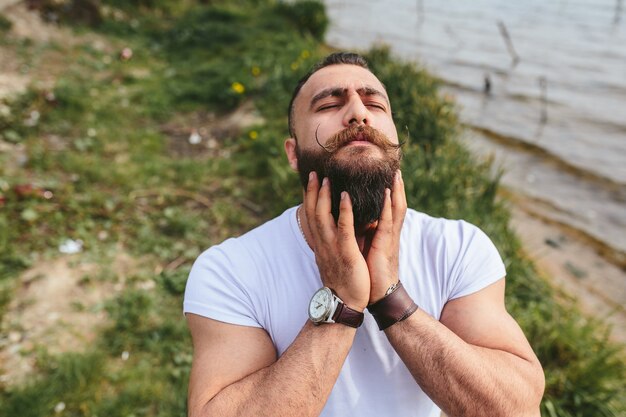 American Bearded Man sieht in einer blauen Jacke am Flussufer aus river